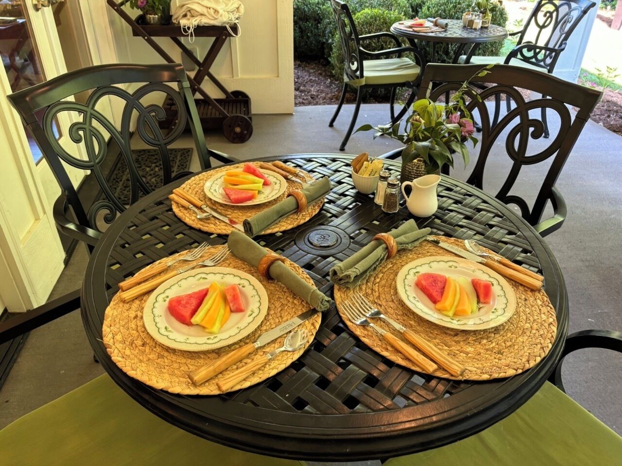 Una mesa redonda dispuesta con platos, cubiertos y servilletas, rodeada de sillas.
