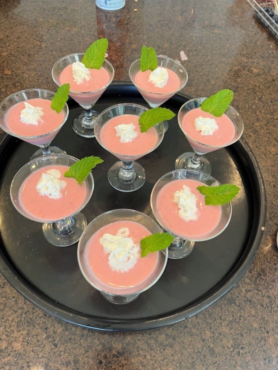 Un plateau contenant six verres de dessert rose, surmontés de crème fouettée et de feuilles de menthe.