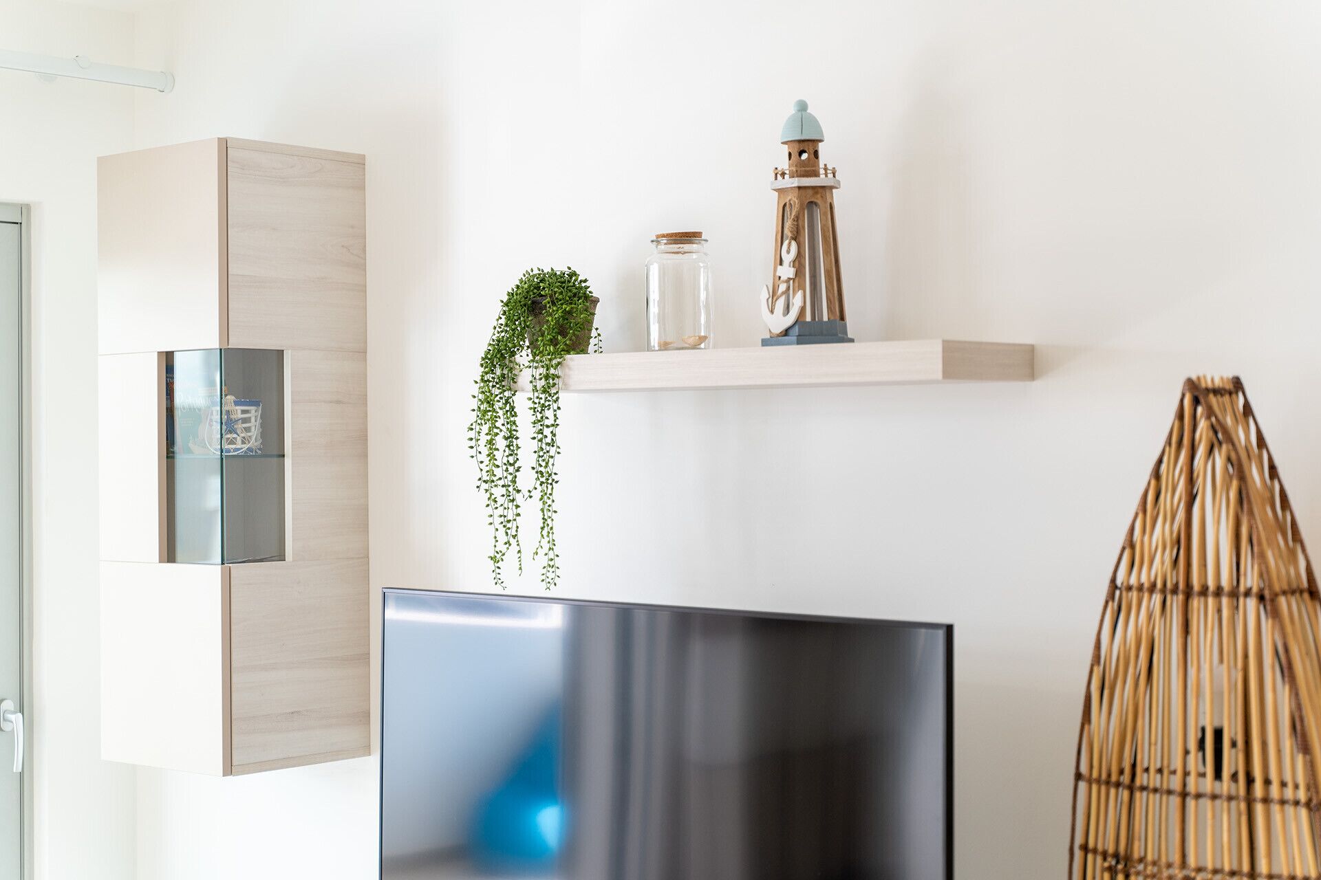 Un salon moderne avec un téléviseur à écran plat, un meuble en bois, une plante suspendue, une lanterne décorative et un panier tressé.