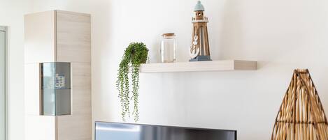 Un salon moderne avec un téléviseur à écran plat, un meuble en bois, une plante suspendue, une lanterne décorative et un panier tressé.