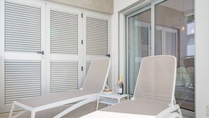 Zwei weiße Lounge-Stühle mit Glastür und Rollläden im Hintergrund.