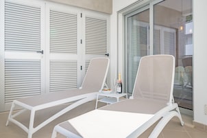 Two white lounge chairs with a glass door and shutters in the background.