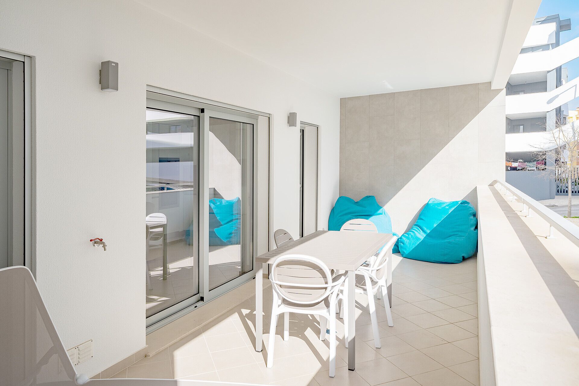 Un balcon avec une table et des chaises pour prendre les repas, une porte-fenêtre coulissante et des poufs bleus.
