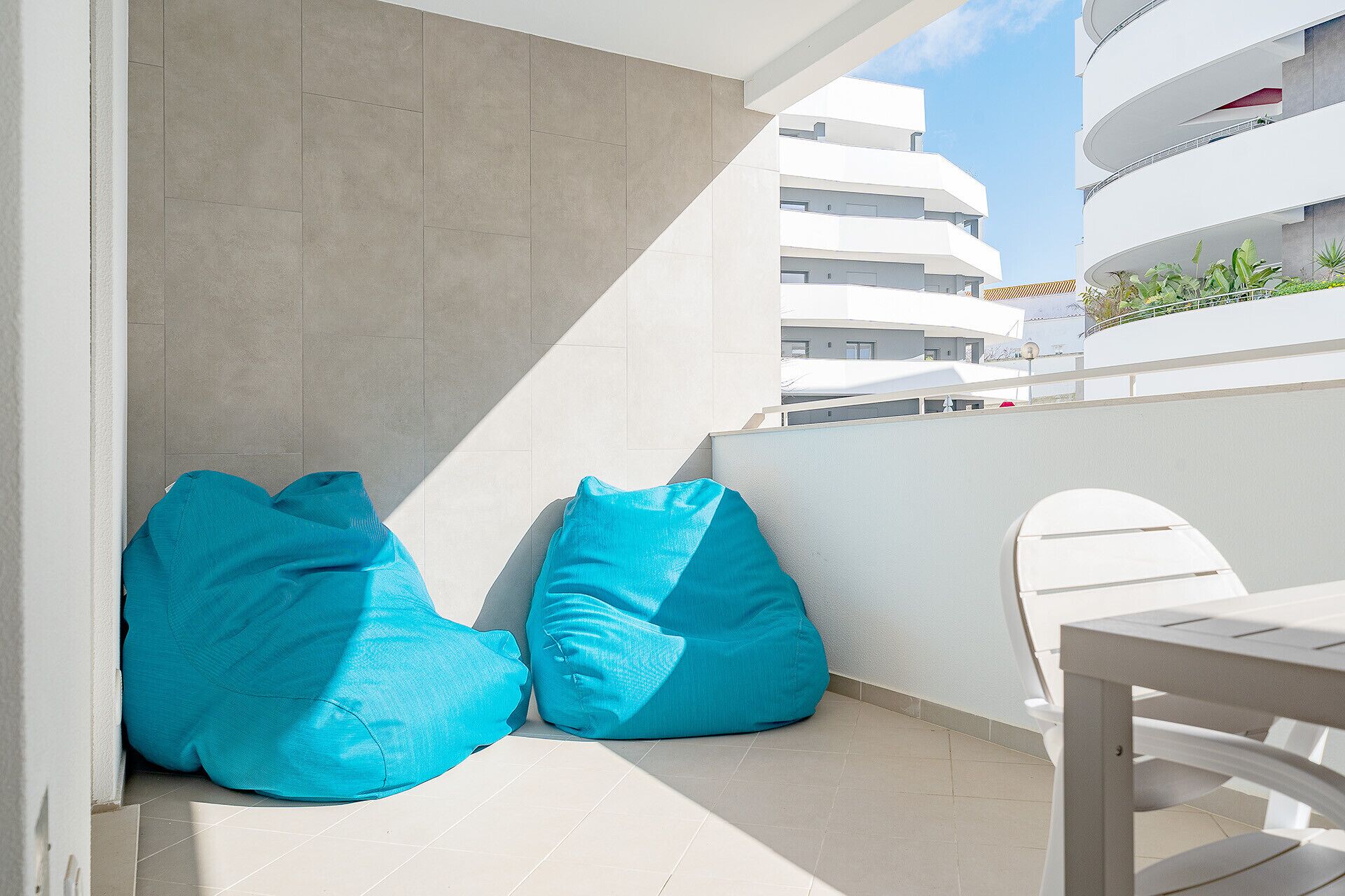 A balcony with two blue bean bags, a white chair, and a view of a modern building.
