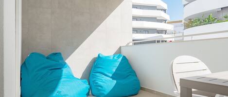 A balcony with two blue bean bags, a white chair, and a view of a modern building.