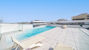 Ein Dachpool mit klarem, blauem Wasser, umgeben von weißen Liegestühlen und einer Glasbrüstung.