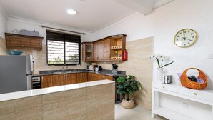 A modern kitchen with a central island, wooden cabinets, a built-in oven, and a window with blinds. - Elegant Apartment with Stunning Nature views. (Kampala)