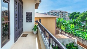 A balcony with a blackboard sign, a potted plant, and a view of surrounding buildings and greenery. - Elegant Apartment with Stunning Nature views. (Kampala)