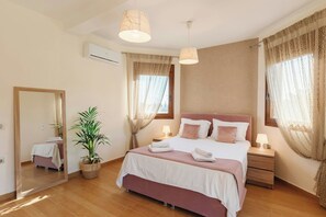 Une chambre à coucher avec un lit, des tables de chevet, un miroir, une plante en pot et une fenêtre avec des rideaux.