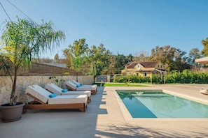 Uma área à beira da piscina com espreguiçadeiras, uma piscina e uma casa ao fundo.