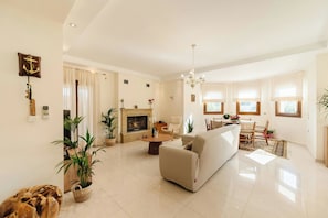 Uma sala de estar espaçosa com lareira, um sofá, um espaço de refeições e um candelabro.