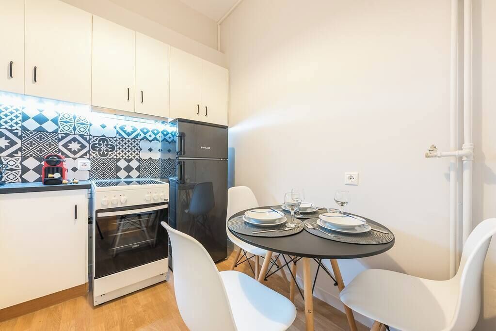 Une cuisine compacte avec des meubles blancs, un réfrigérateur noir et une petite table à manger pour deux personnes.