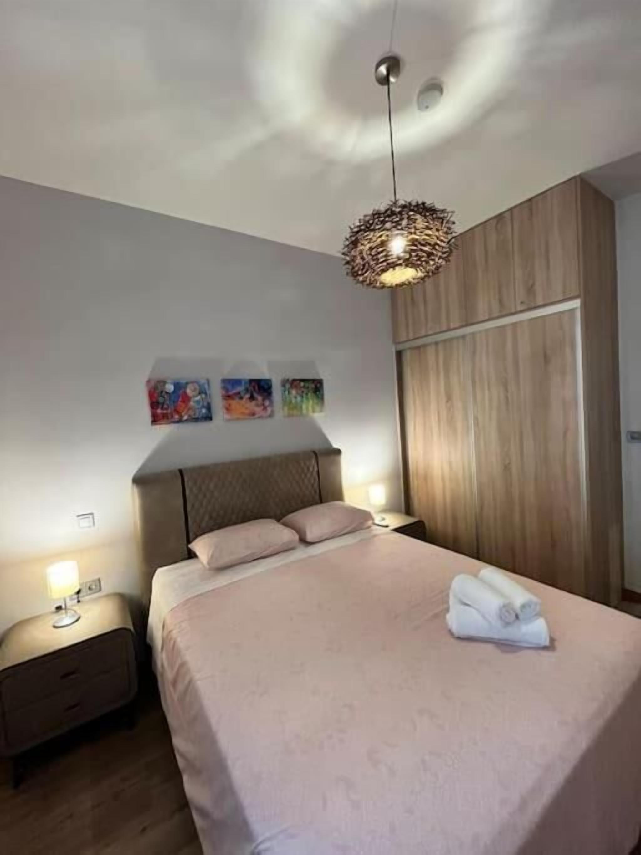 Une chambre à coucher comprenant un lit, des tables de chevet, une armoire en bois et un luminaire au plafond original.
