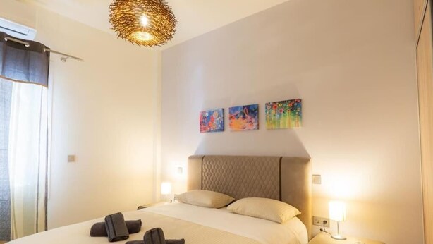 A hotel room with a bed, two bedside lamps, a headboard, and three wall art pieces. - Panathenaic Stadium Apartment by Greece Apartments (Athens)