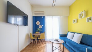Ein Wohnzimmer mit einem blauen Sofa, einem kleinen runden Tisch und einem an der Wand befestigten Fernseher.