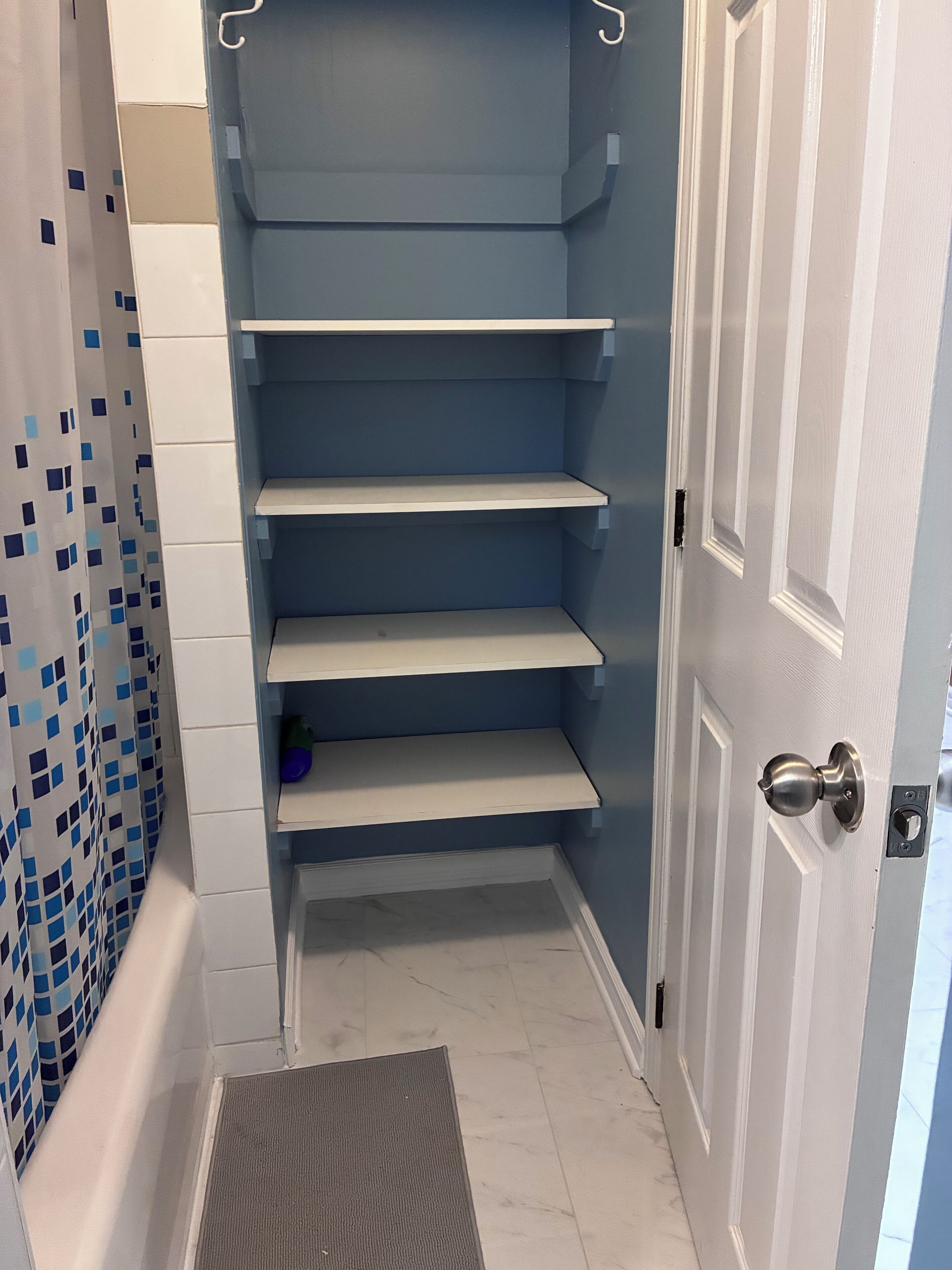 Un bagno con parete rivestita in piastrelle blu, una porta bianca e zona doccia con tenda a scacchi blu e bianchi.