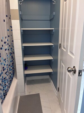 Een badkamer met een blauw betegelde muur, een witte deur en een douchegedeelte met een blauw-wit geruit douchegordijn.