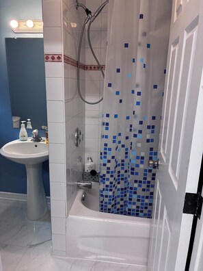 Et badeværelse med badekar, håndvask og bruser.