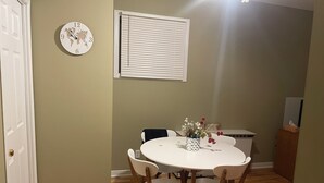 A dining area with a round table, four chairs, a clock, and a window with blinds. - Monthly rental - 1-BDR apt, ALL included (hot water, hydro and heating). (Ottawa)
