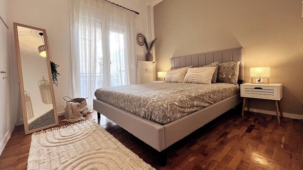A bedroom with a large bed, bedside tables, a mirror, and a window with curtains.