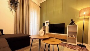 A modern living room with a sofa, two round tables, a TV, and a bookshelf with the letters "GA".