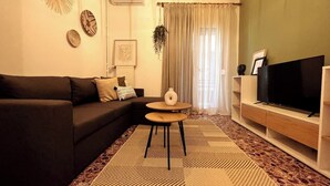 A living room with a dark sofa, a round coffee table, a flat-screen TV, and a patterned rug.