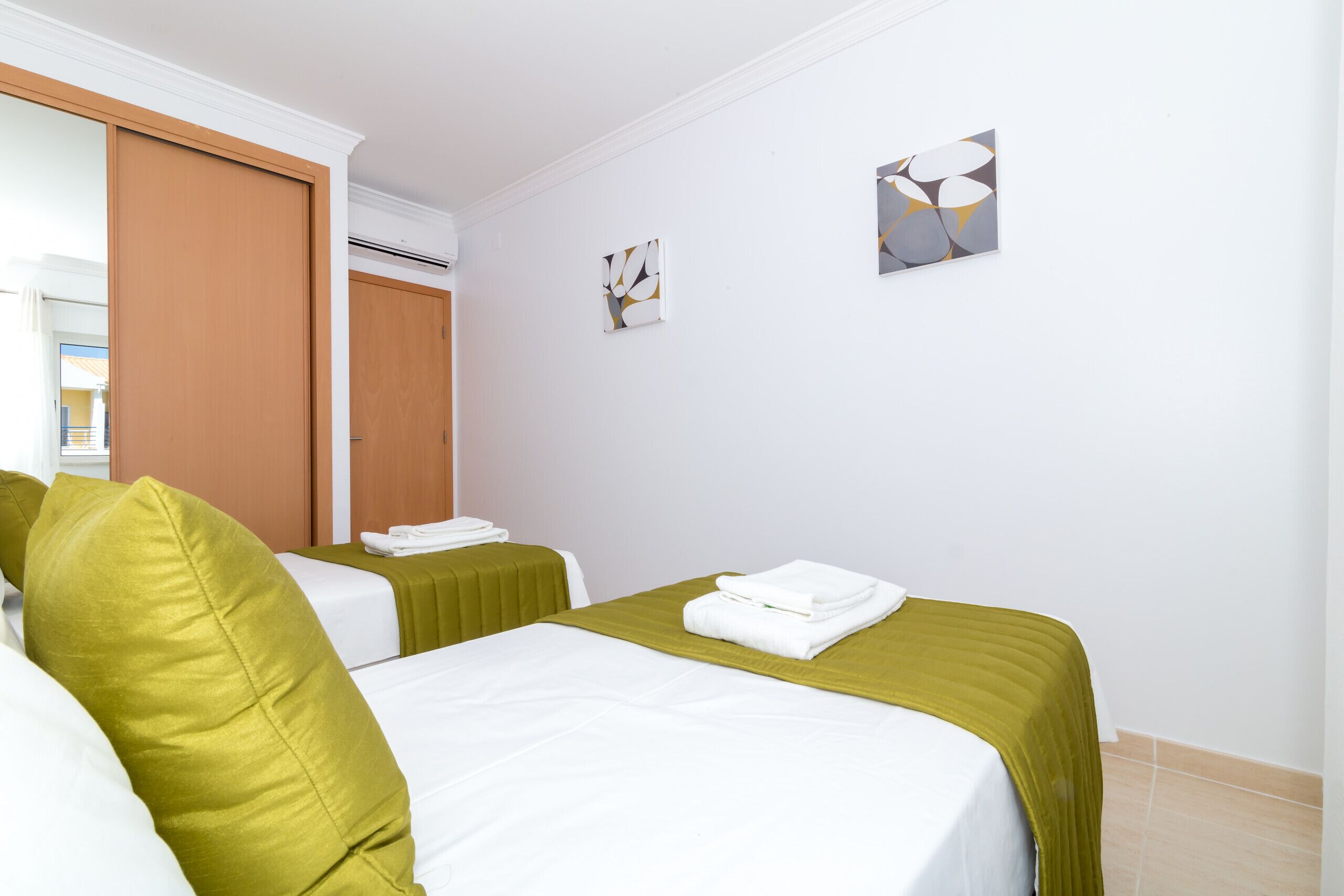 Una camera d'albergo con due letti, ognuno con biancheria verde e cuscini bianchi, un piccolo quadro appeso al muro e una porta in legno.