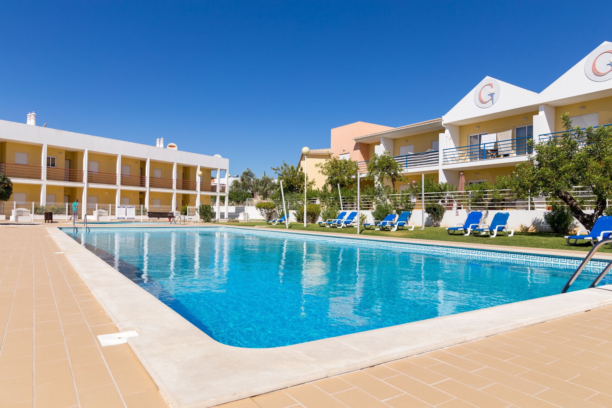 A swimming pool with blue water, surrounded by lounge chairs and a building with balconies.