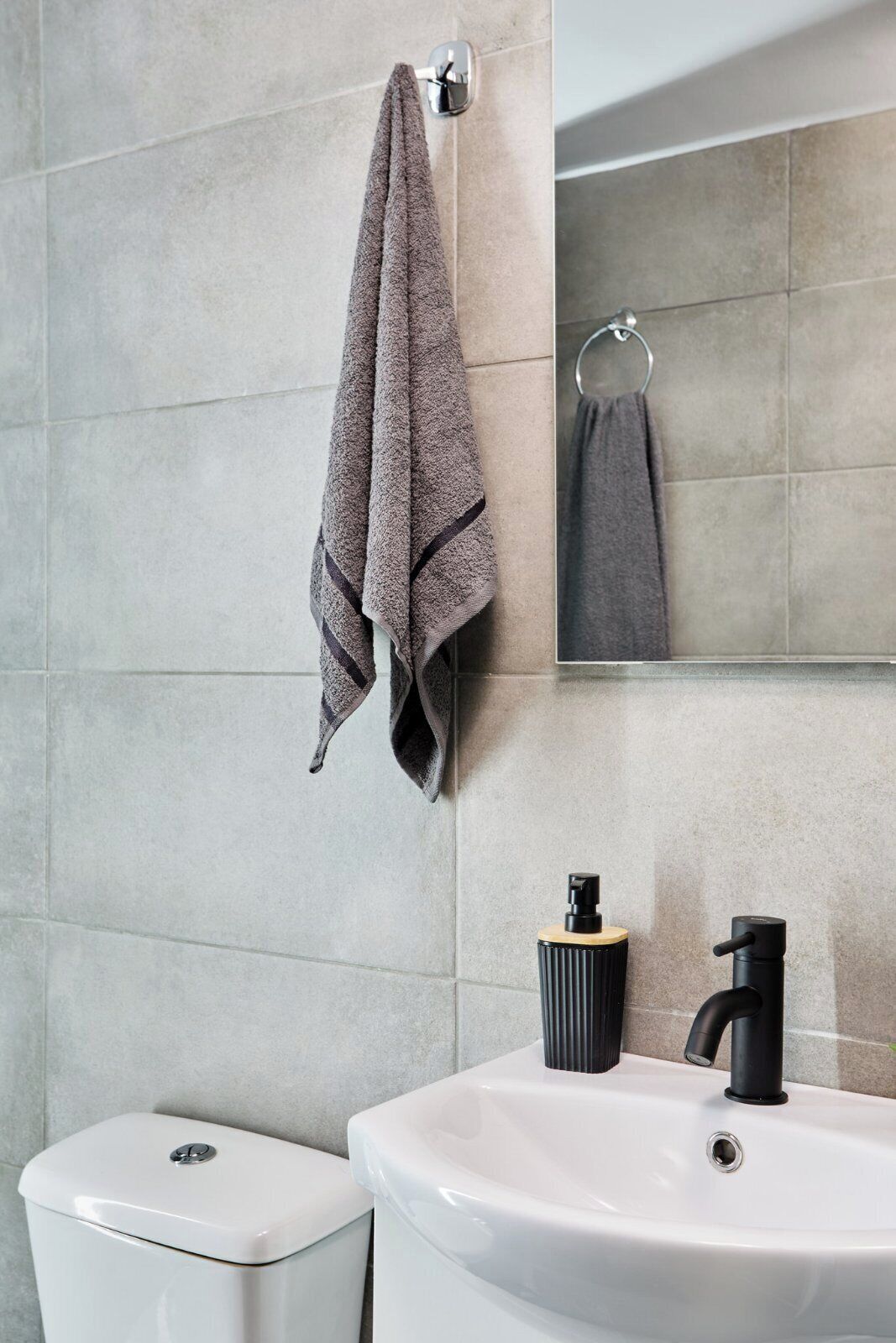 A bathroom with a toilet, a sink with a black faucet, and a towel hanging on a towel rack.