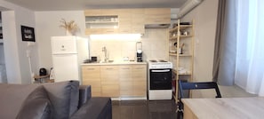 A compact kitchen with a refrigerator, stove, and wooden cabinets. There is a dining area with a table and chairs. - West Garden in Aigio (Aigio)