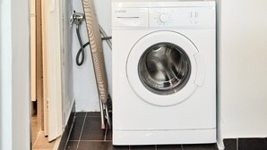 A compact laundry area with a front-loading washing machine, a hanging rack, and potted plants on shelves. - West Garden in Aigio (Aigio)