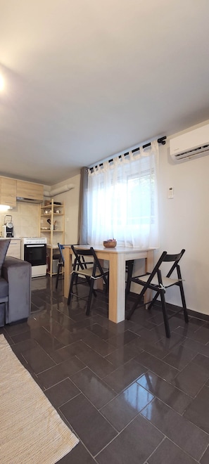 A modern kitchen with a built-in oven, a dining table with four chairs, and a window with sheer curtains. - West Garden in Aigio (Aigio)