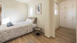 Un dormitorio con cama, mesita de noche con lámpara, armario y un cuadro en la pared.