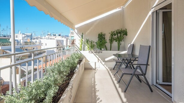 Un balcón con mesa y sillas, plantas en macetas y vistas de la ciudad.