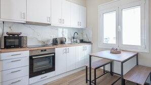 Una cocina moderna con armarios blancos, horno empotrado, microondas y cafetera. Hay una ventana con vistas al exterior.