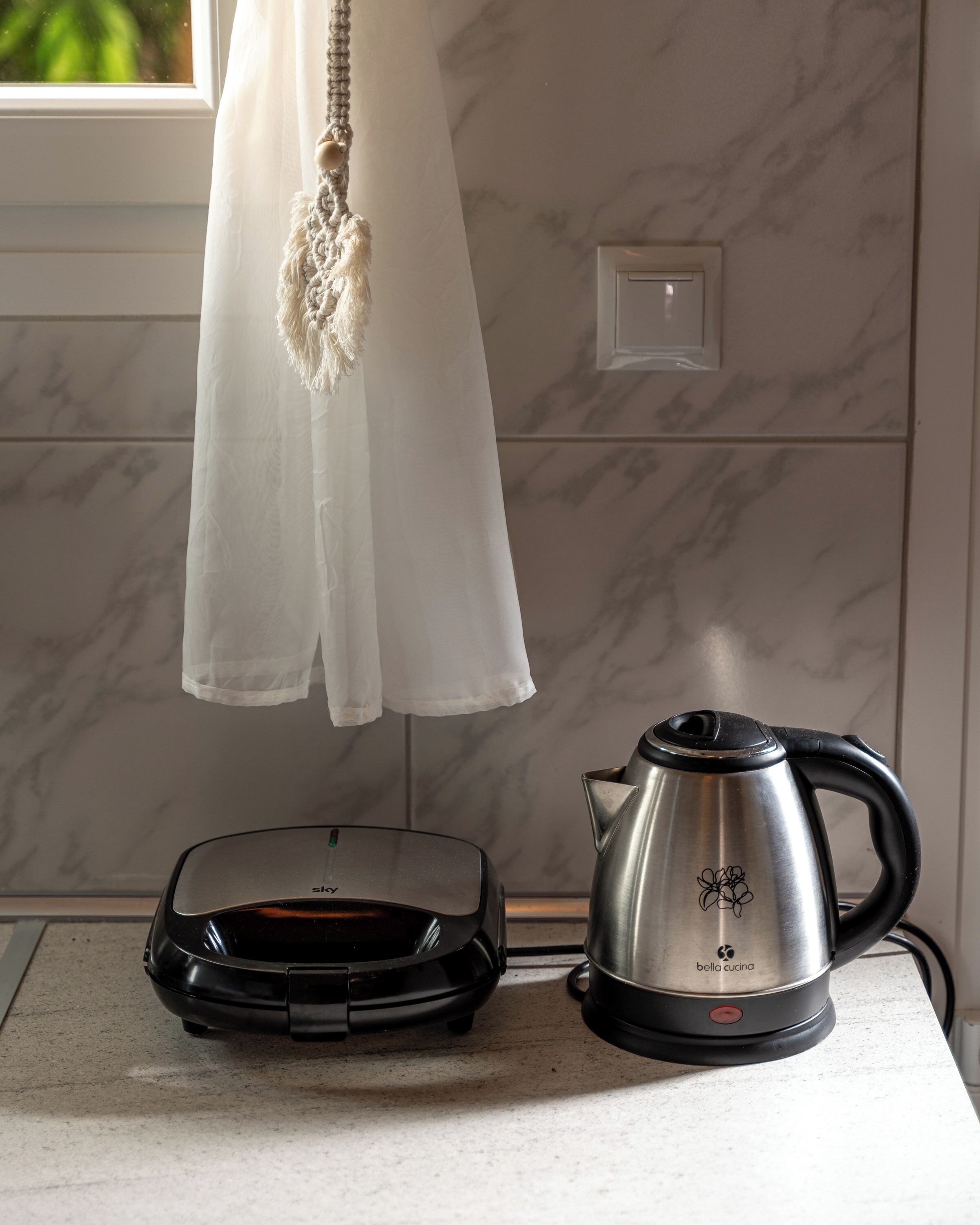 A kitchen with a toaster, kettle, and a white curtain.