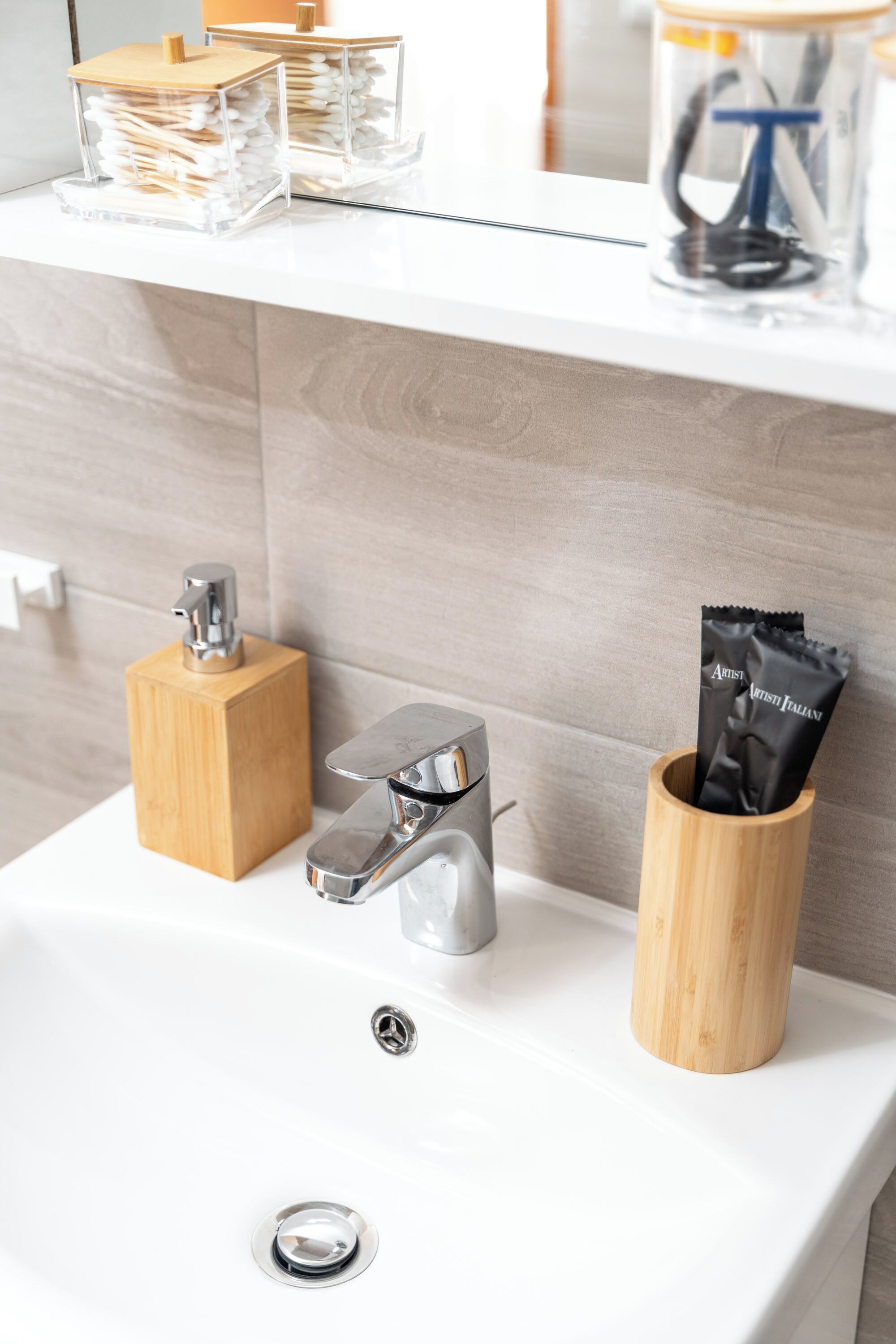 Een moderne wastafel met een chromen kraan, een houten zeepdispenser en een houten beker met toiletartikelen.