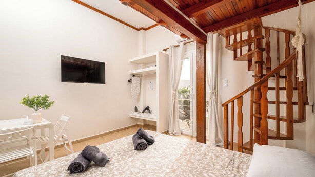 A bedroom with a bed, a desk, a chair, a TV, and a wooden staircase.