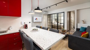 A modern kitchen with red cabinets, a white countertop, and a dining area with a table and chairs. - Alkis Luxury By Greece Apartments (Zografou)