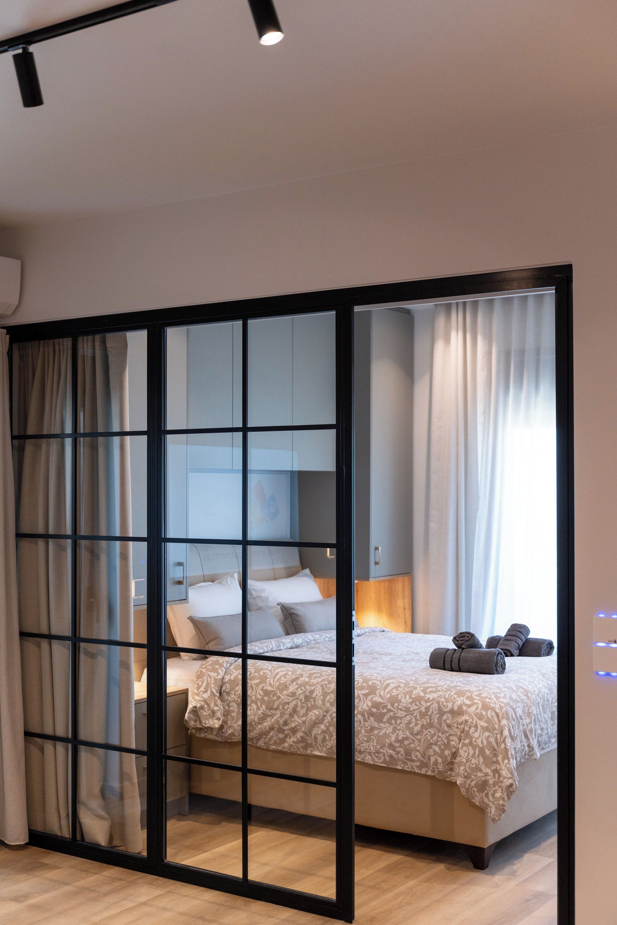 A modern bedroom with a sliding glass door, a bed with a patterned bedspread, and a bedside table with a lamp.