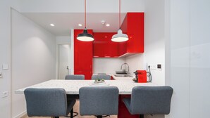 A modern kitchen with red cabinets, a white countertop, and three grey chairs. - Alkis Luxury By Greece Apartments (Zografou)