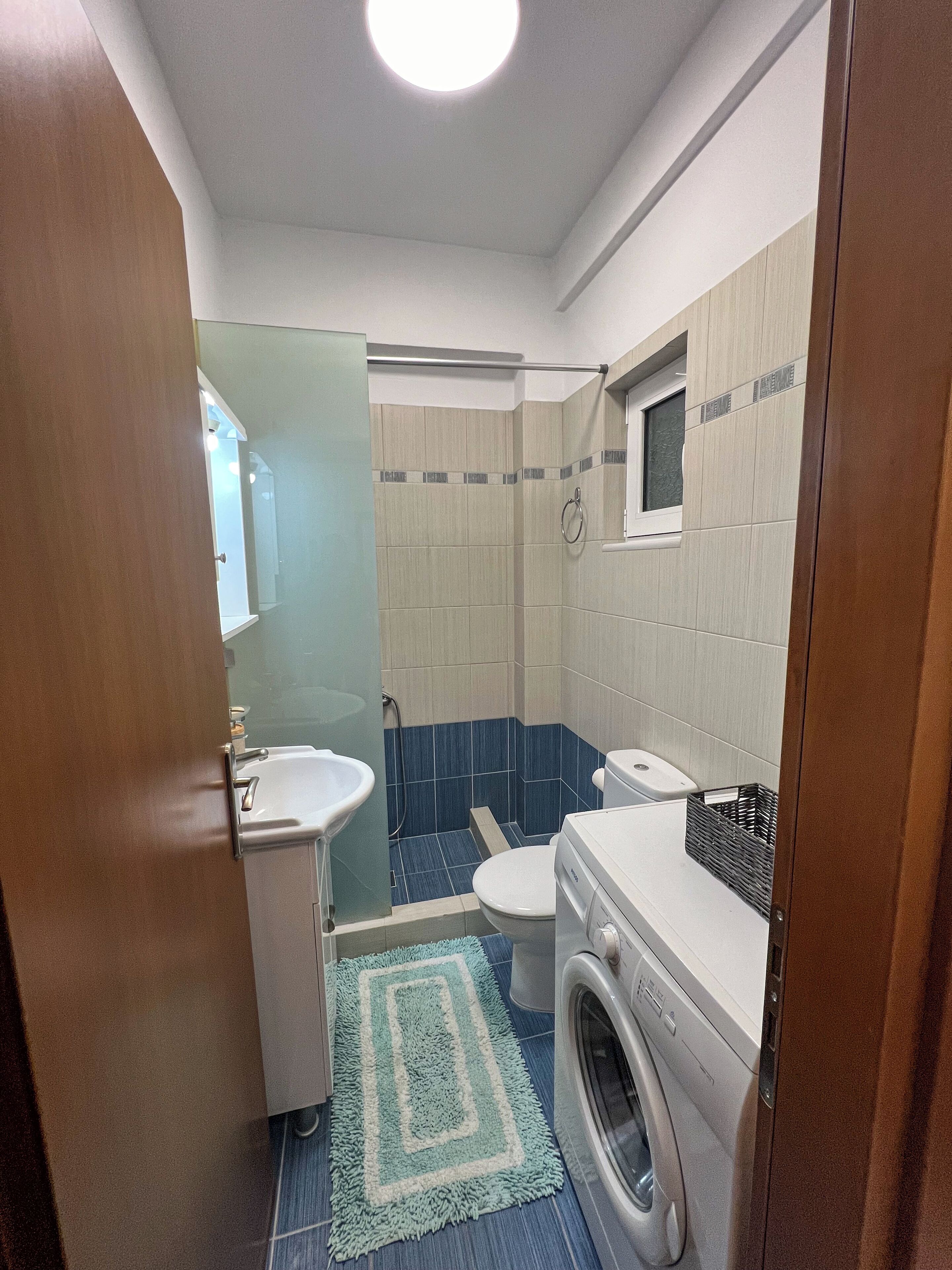 Un baño pequeño con lavamanos, inodoro, ducha y lavadora.