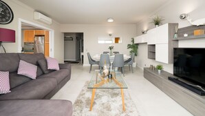 A modern living room with a grey sofa, a glass coffee table, and a dining area with a white table and grey chairs. - Lagos Terrace With Pool by Homing (Lagos)
