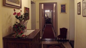 A hallway with a chandelier, a vase of flowers, and framed pictures on the walls. - Anna (Perugia)