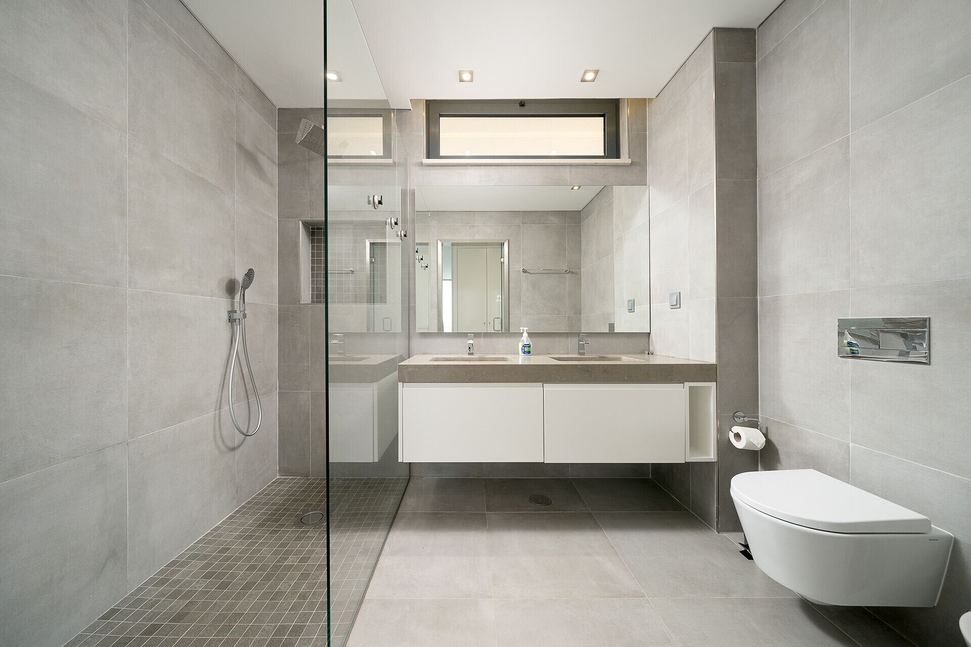A modern bathroom with a glass-enclosed shower, a double sink vanity, and a toilet.