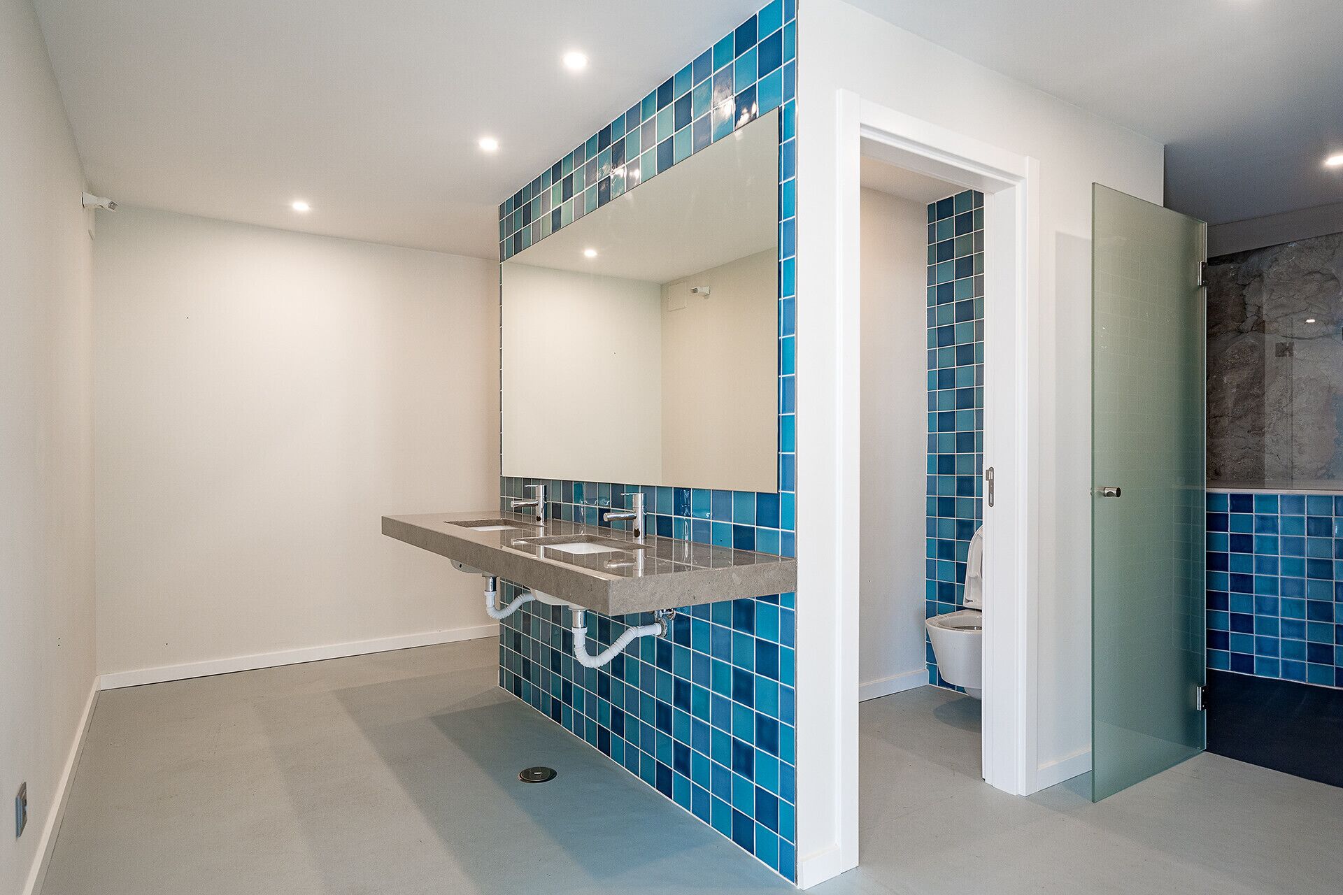 Une salle de bain avec deux lavabos, un grand miroir et des murs recouverts de carreaux bleus.