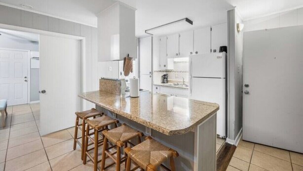 A modern kitchen with white cabinets, a granite countertop, and wooden stools. - Serene Midtown Cottage - Walk to Hotspots! (Mobile)