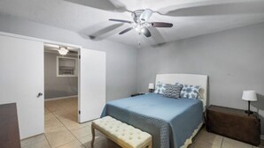 A bedroom with a bed, a bench, a suitcase, a ceiling fan, and an open door leading to another room. - Serene Midtown Cottage - Walk to Hotspots! (Mobile)