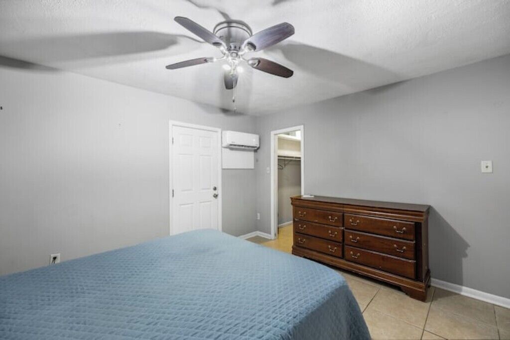 A bedroom with a bed, a dresser, a ceiling fan, and an air conditioning unit.