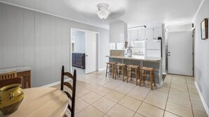 A compact kitchen with a dining area, featuring a central island with stools, a refrigerator, and a microwave. - Serene Midtown Cottage - Walk to Hotspots! (Mobile)